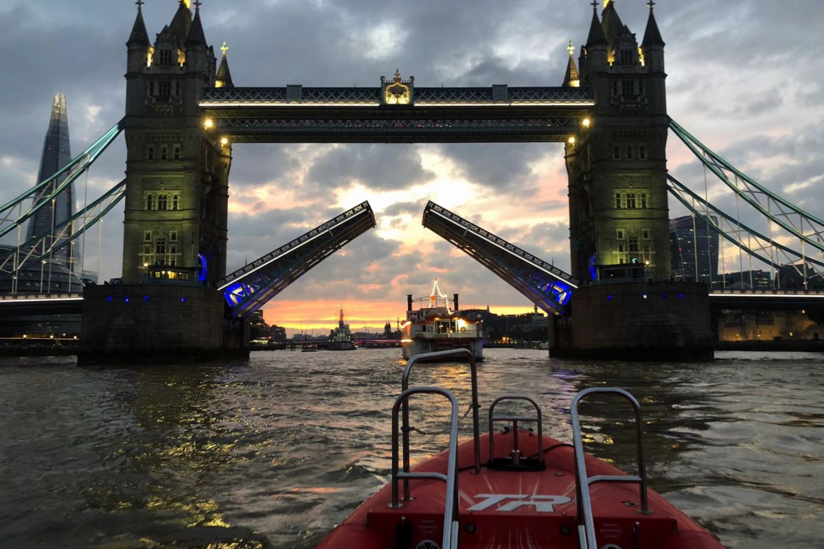 Tower Bridge lit by lights, lifting at sunset to allow boats through.